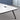 White rounded rectangular meeting table with a black edge, splayed black legs and two cable ports, visible surface detail in the same office